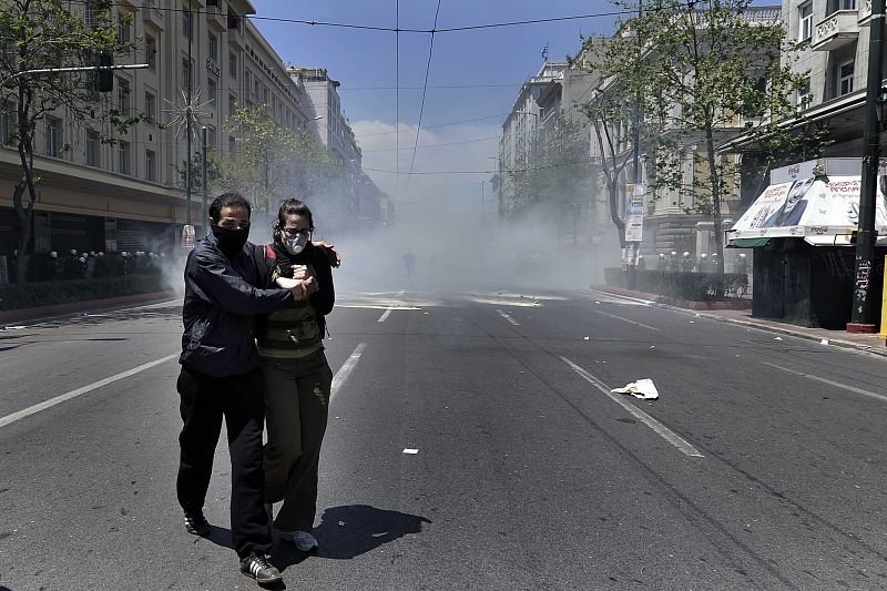 Dos manifestantes huyen de los gases lacrimógenos lanzados por la policía en Atenas