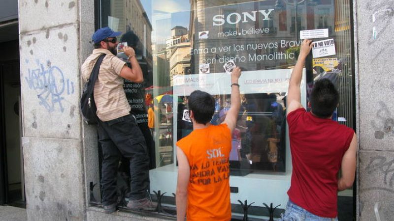 Tres jóvenes acampados limpian los escaparates de unos grandes almacenes.