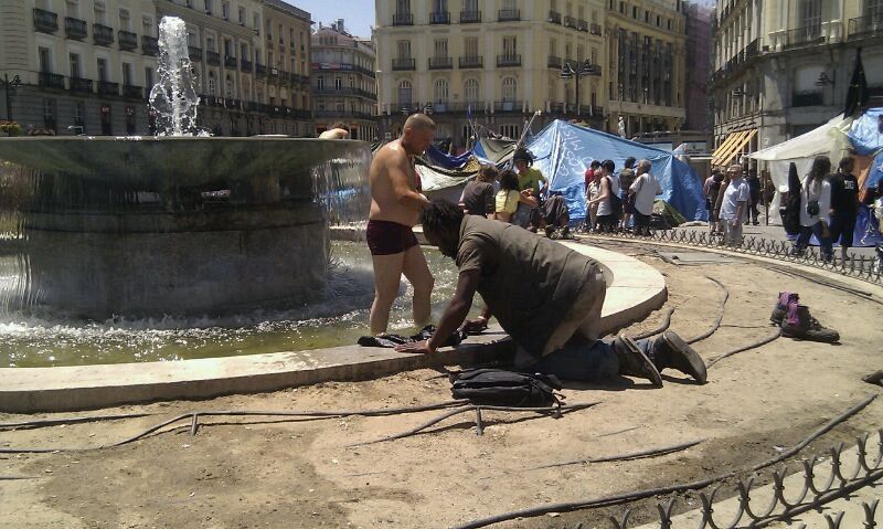 Dos hombres se asean y lavan su ropa en una de las fuentes de la Puerta del Sol.