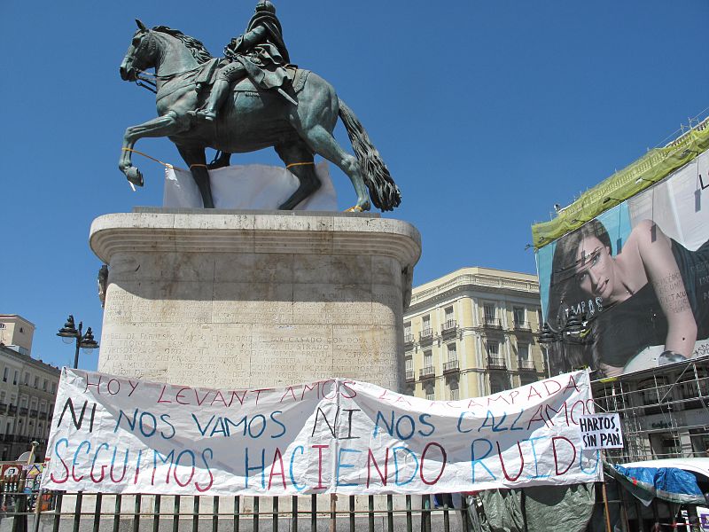 Pancarta en la estatua de Carlos III: "Hoy levantamos la acammpada. Ni nos vamos ni nos callamos. seguimos haciendo ruido".