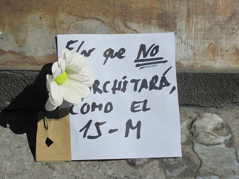 Mensaje al lado de la placa anterior, debajo de la estatua de Carlos III, en laPuerta del Sol: "La flor que no marchitará, como el 15M".
