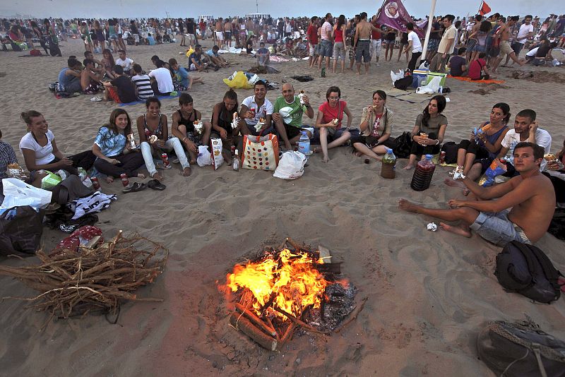 Un grupo de jóvenes cena junto a una hoguera en la playa valenciana de la Malvarrosa.