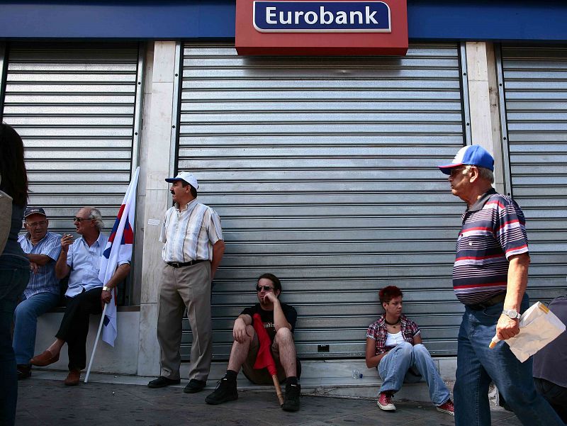 Varios manifestantes sentados frente a una entidad bancaria cerrada por la jornada de huelga