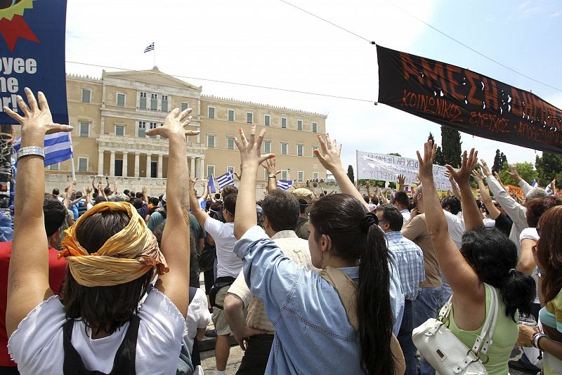Unos manifestantes llevan pancartas y banderas griegas mientras elevan sus manos y gritan consignas frente al Parlamento