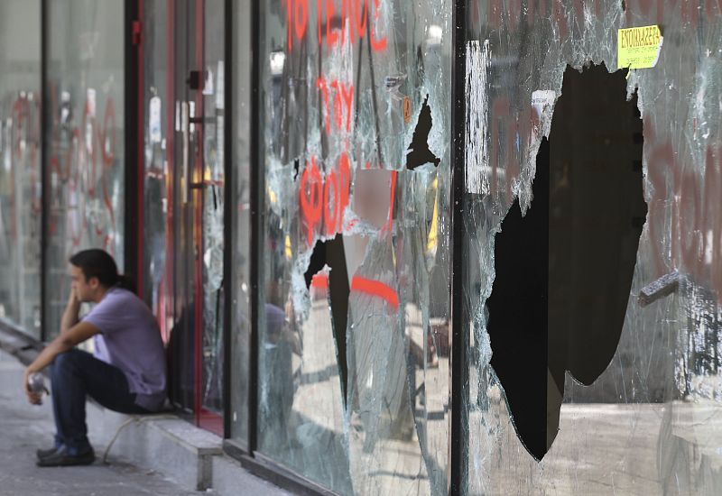 Un hombre habla por teléfono junto a un escaparate destrozado tras dos días de violentos enfrentamientos en la plaza Syntagma en Atenas.