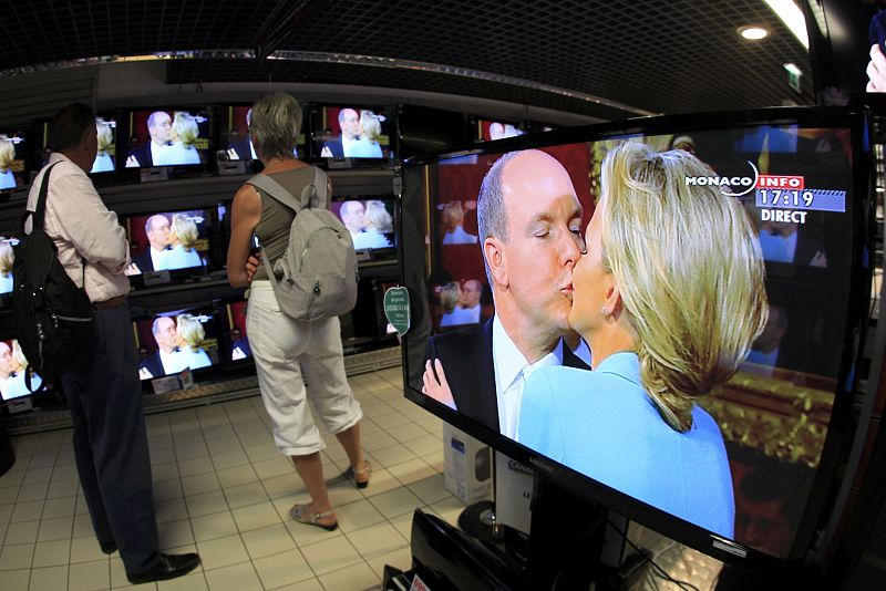 Una pareja ve a través de las televisiones de una tienda el momento en el que la pareja se besa.