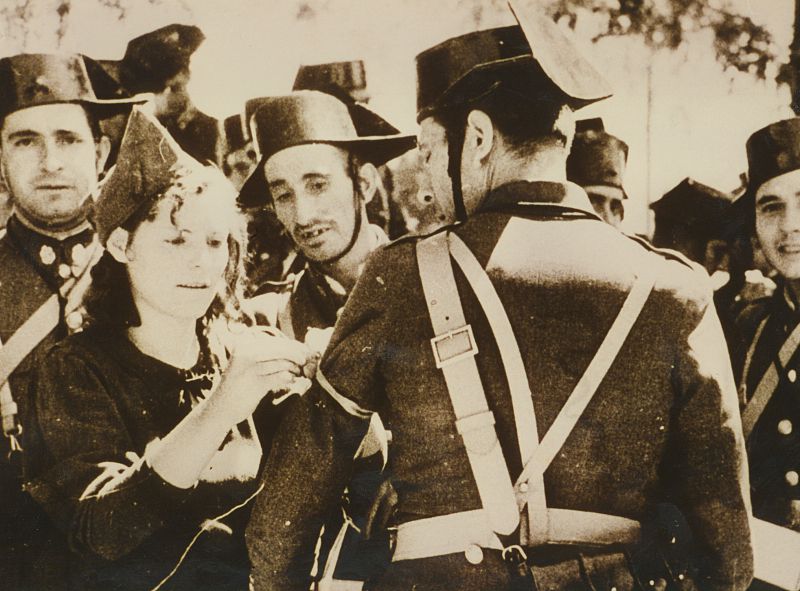 Una mujer, poniendo un banderín a un guardia civil durante la guerra