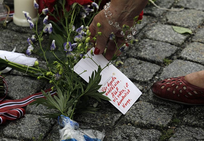A woman places a postcard on the cobble stones of the market square outside the Oslo cathedral to mourn the victims of a bomb blast and a rampage