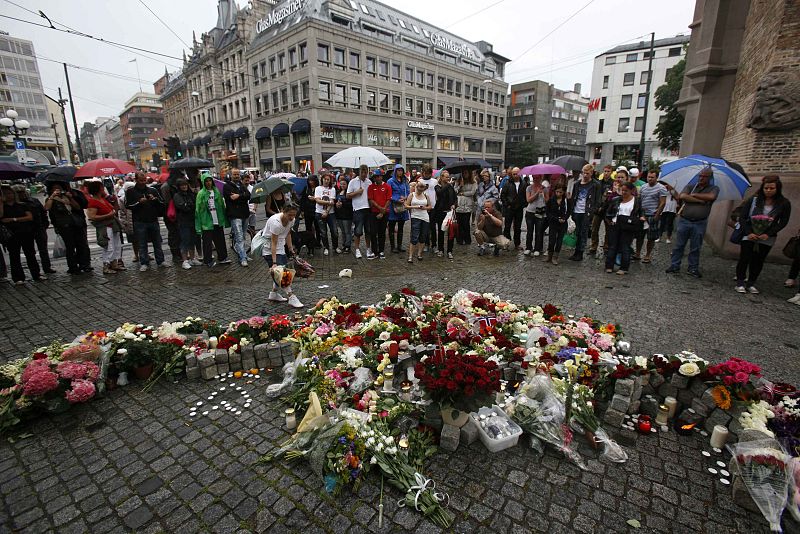 A woman places flowers on the market square outside the Oslo cathedral as others mourn the victims of a bomb blast and a rampage in Norway