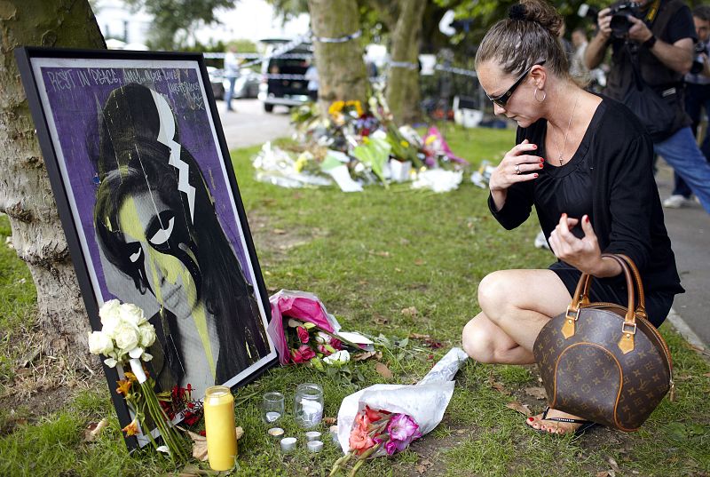 Una mujer se arrodilla ante una imagen de la fallecida cantante Amy Winehouse. Cientos de seguidores se han acercado a Camden, donde residía, para decirle adiós.