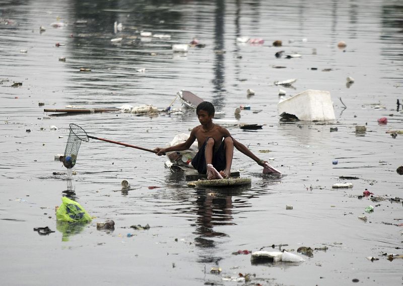 Un niño filipino usa una tabla para flotar a causa de las inundaciones, en la Ciudad de Las Pinas