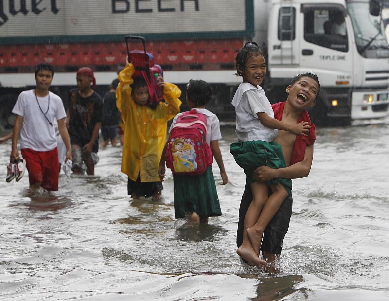 Un niño lleva a su hermana menor en brazos para cruzar las calles inundadas de Malabón, al norte de Manila