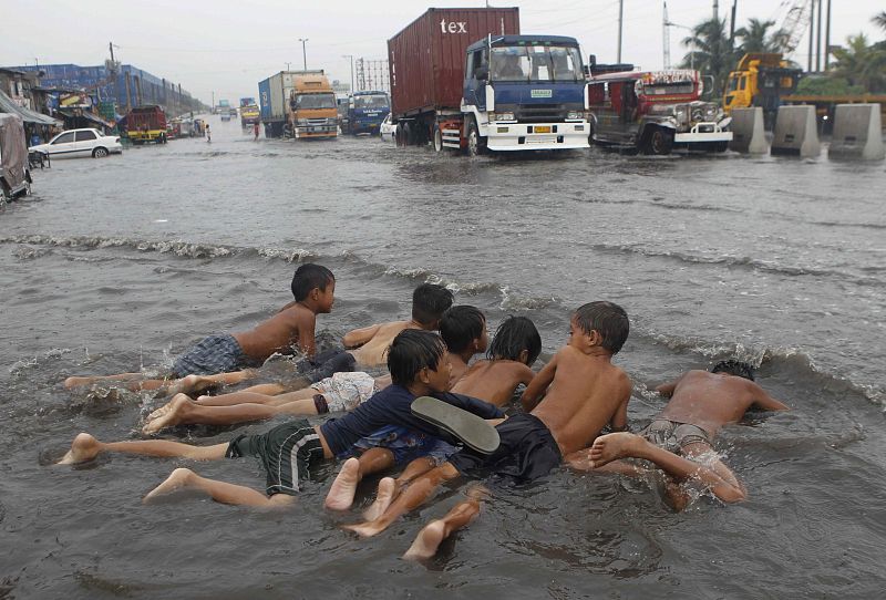 Unos niños juegan en el agua que ha dejado en las calles el tifón Nock-Ten