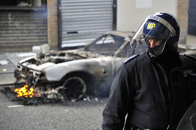 Un antidistubios se pone delante de un coche en llamas en el tecer día consecutivo de protestas.