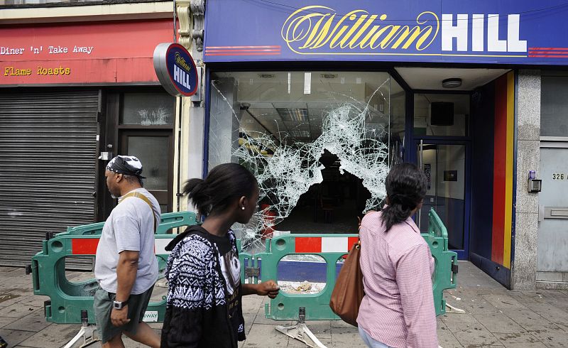 Personas observan los daños provocados en el escaparate de un comercio en Tottenham.