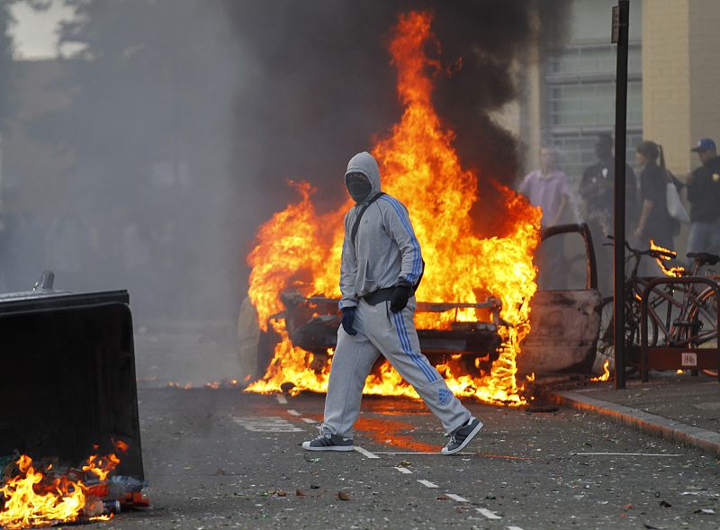 Un hombre encapuchado cruza una calle cortada por contenedores ardiendo, en el conflictivo barrio de Hackney.