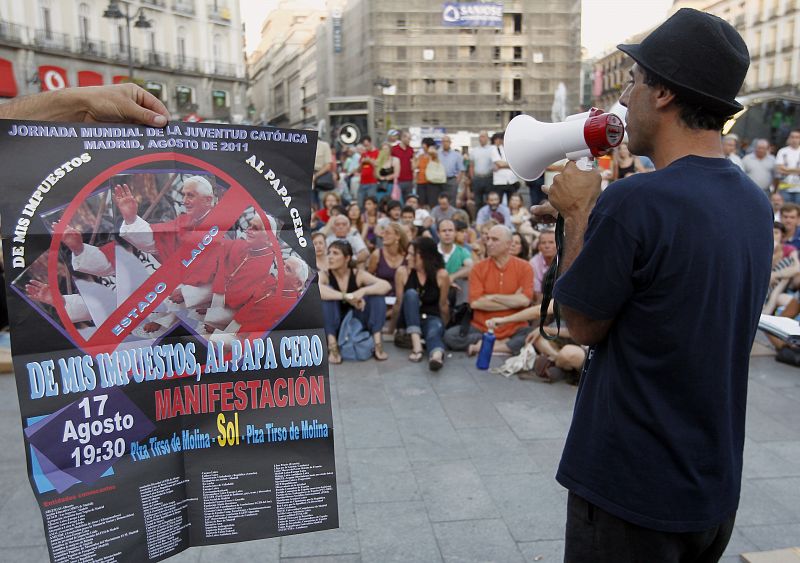 Un cartel en contra de la visita del papa Benedicto XVI con motivo de la Jornada Mundial de la Juventud 2011 es mostrado durante una asamblea del Movimiento 15M