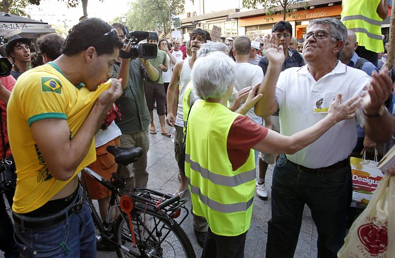 Un peregrino besa su camiseta mientras uno de los manifestantes le exhorta los elevados costes de la visita del papa.