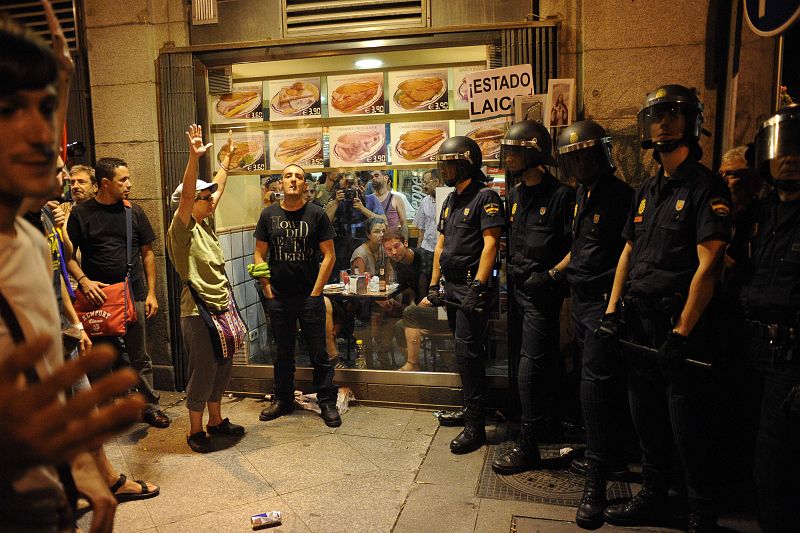 Varios manifestantes frente a la policía protestan por el uso de fondos públicos en la visita del Papa