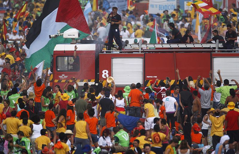 Un bombero refresca a los peregrinos que están aguantando temperaturas muy altas durante la espera en Cuatro Vientos
