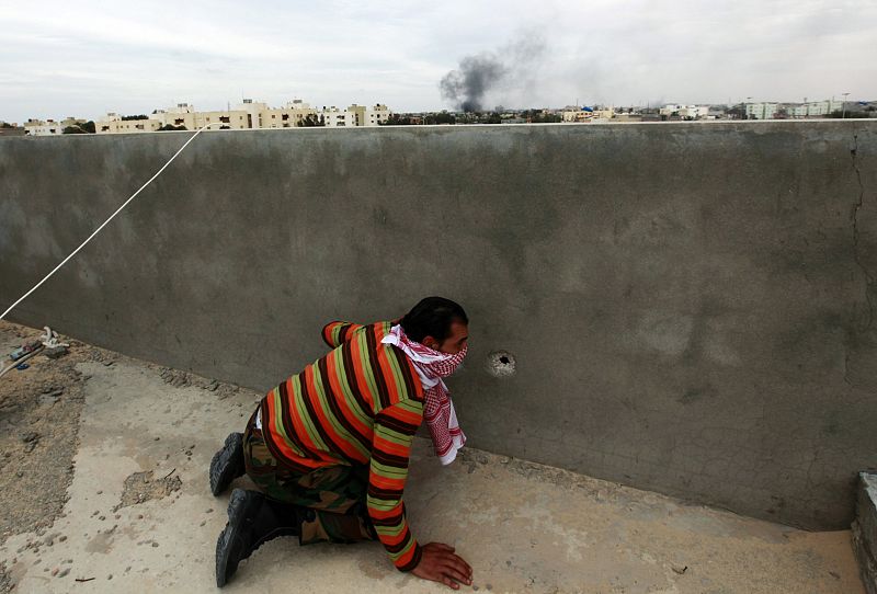 Un rebelde se esconde tras un muro y mira a través de un agujero causado por el impacto de una bala durante un bombardeo cerca de Trípoli.