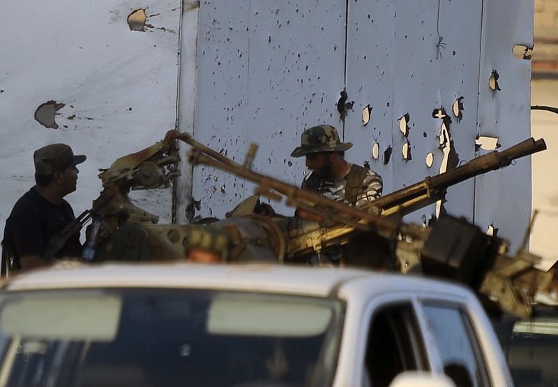 Rebeldes libios delante de un panel agujereado por los impactos de bala durante el enfrentamiento que ha tenido lugar hoy en Trípoli.