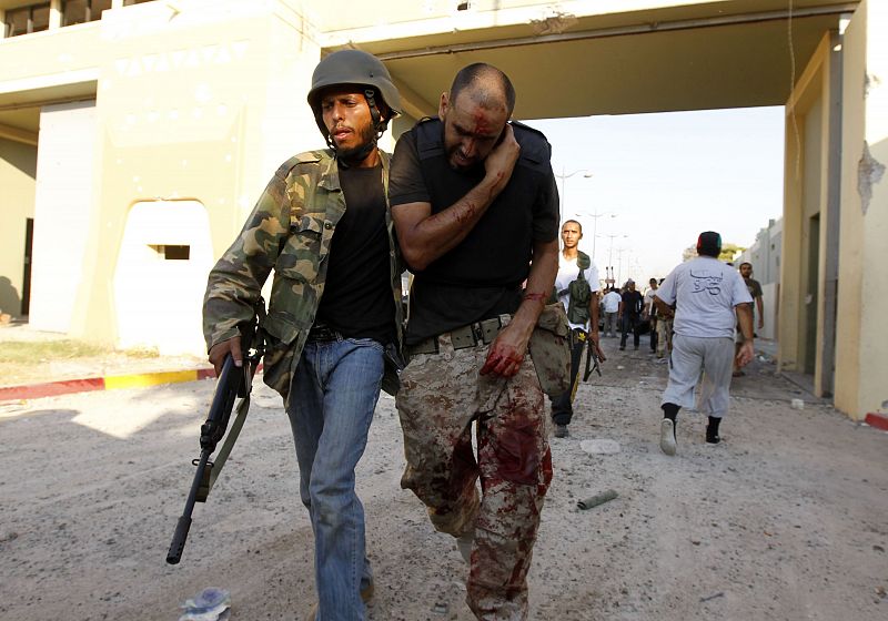 Libyan rebel assists an injured fellow rebel at Bab Al-Aziziya compound in Tripoli