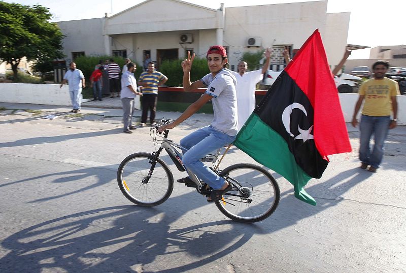 Un jóven lleva en un bicicleta la nueva bandera del Reino de Libia por las calles de Janzour