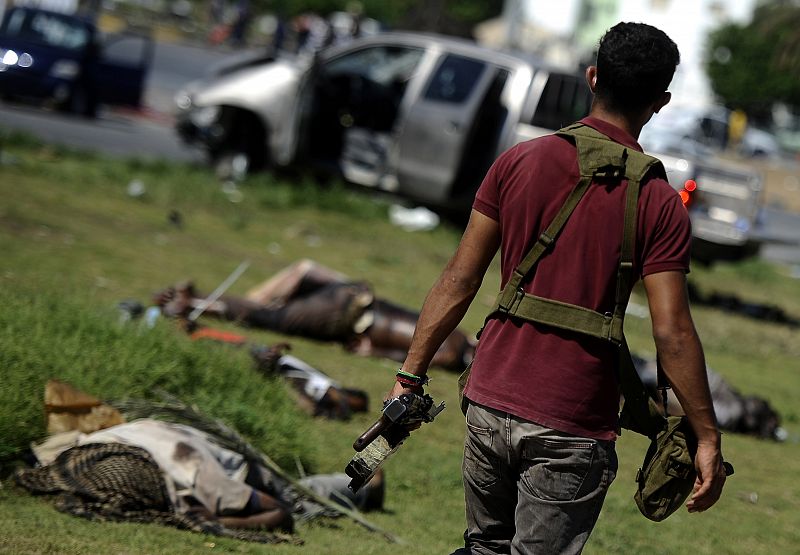 Un rebelde camina entre los cuerpos de combatientes leales a Gadafi