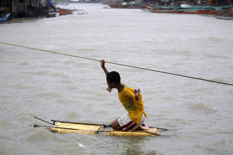 Un hombre cruza una calle anegada por un río de Manila a causa de las inundaciones que causa el tifón