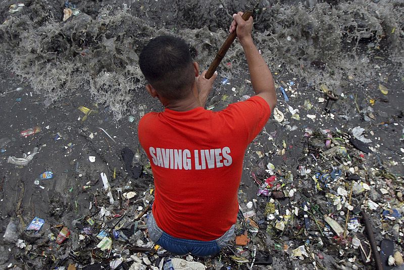 Un guardia costero, con una camiseta que dice 'Salvando vidas' limipia la orilla de la bahía de Filipinas