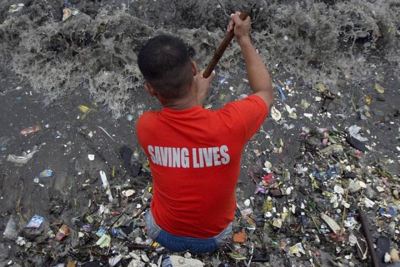 Un guardia costero, con una camiseta que dice 'Salvando vidas' limipia la orilla de la bahía de Filipinas