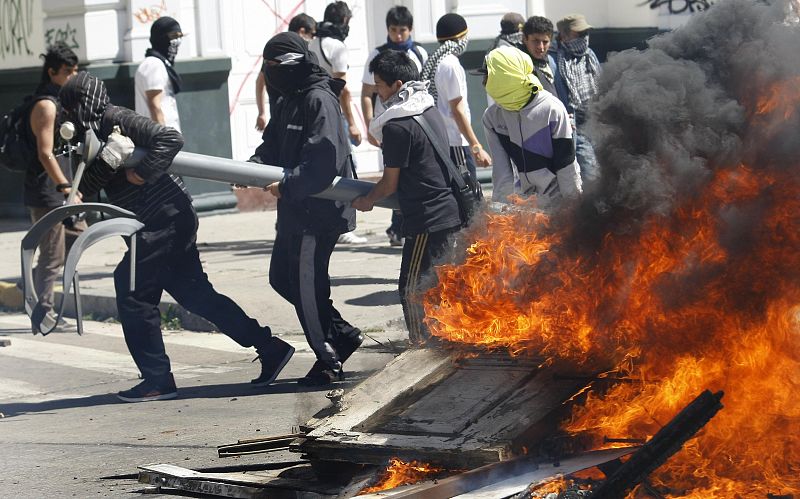 Los manifestantes llevan una varandilla de metal y pasan por una de las barricadas que se han organizado durante las manifestaciones