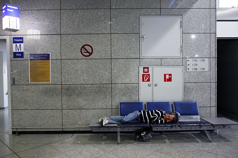 Un pasajero duerme en un banco de la terminal de salidas del aeropuerto de Atenas