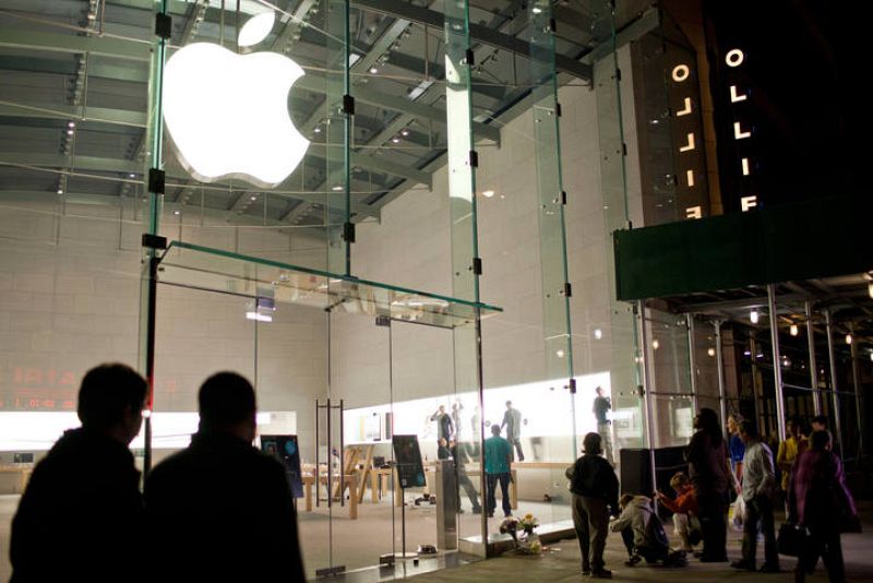 Un grupo de personas observa flores y velas colocadas en memoria de Steve Jobs. 