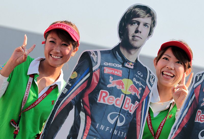 Dos azafatas posan junto a la imagen del piloto alemán de Red Bull Sebastian Vettel