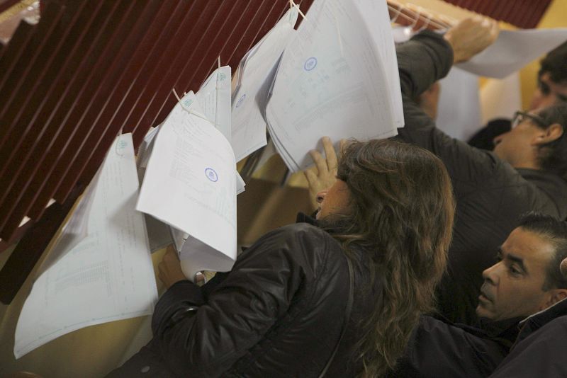 Varios ciudadanos consultan en las listas de un colegio electoral de Madrid la mesa en la que deben votar.
