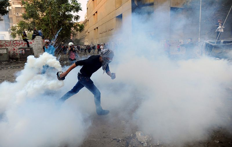 Un manifestante trata de librarse de un bote de gas lacrimógeno durante los enfrentamientos con la policía y soldados