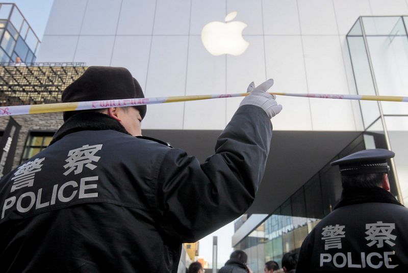 Policías chinos acordonan el exterior de una tienda Apple mientras un grupo de personas espera comprar el nuevo iPhone 4S