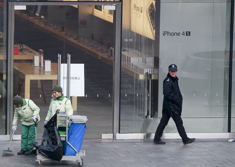 Un policía observa a trabajadores que limpian en el exterior de una tienda Apple después de los incidentes provocados por un grupo de personas que hacía cola comprar el nuevo iPhone 4S