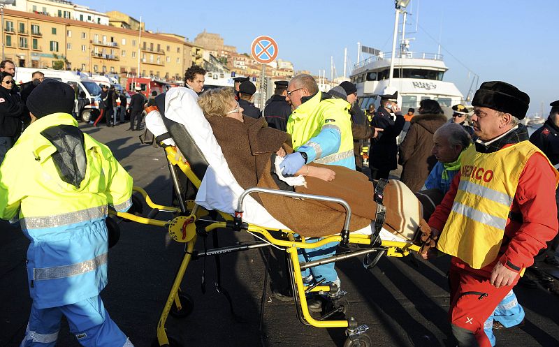 Rescue workers help woman as they arrive at Porto Santo Stefano after cruise ship ran aground off the west coast of Italy at Giglio island