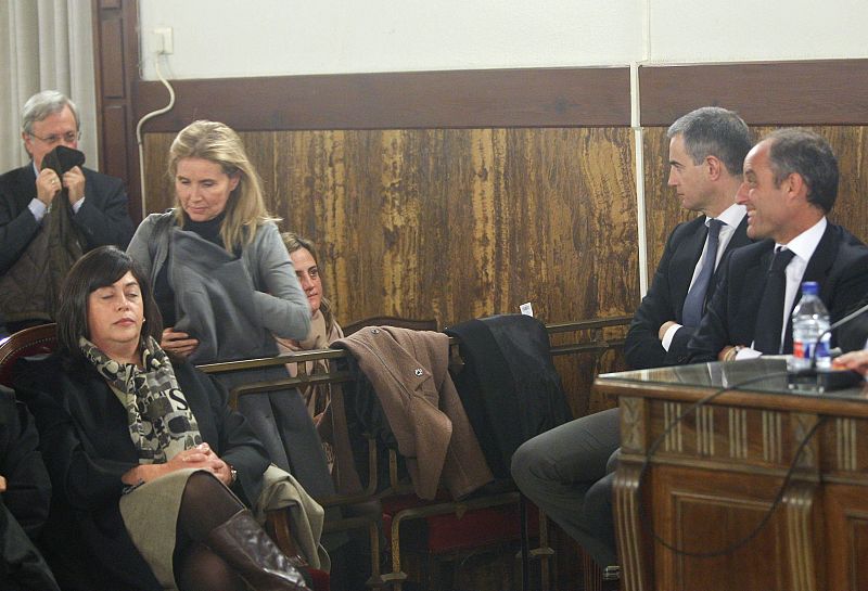 Francisco Camps y Ricardo Costa, sonríen a la esposa de Camps, Isabel Bas (de pie), durante la lectura del veredicto de la denominada causa de los trajes del caso Gürtel.