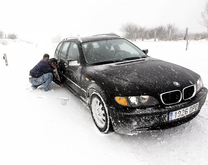 Dos conductores intentan poner cadenas a su coche atrapado en medio de una nevada en Cantabria