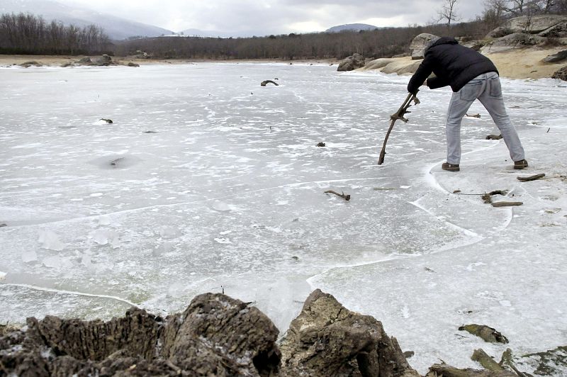 Un hombre intenta romper la gruesa capa de hielo que cubre el pantano del Pontón Alto en Segovia