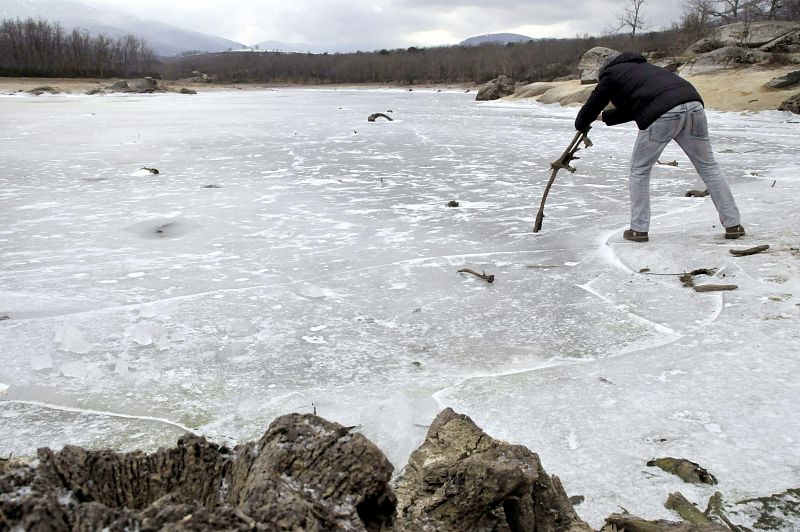 Un hombre intenta romper la gruesa capa de hielo que cubre el pantano del Pontón Alto en Segovia