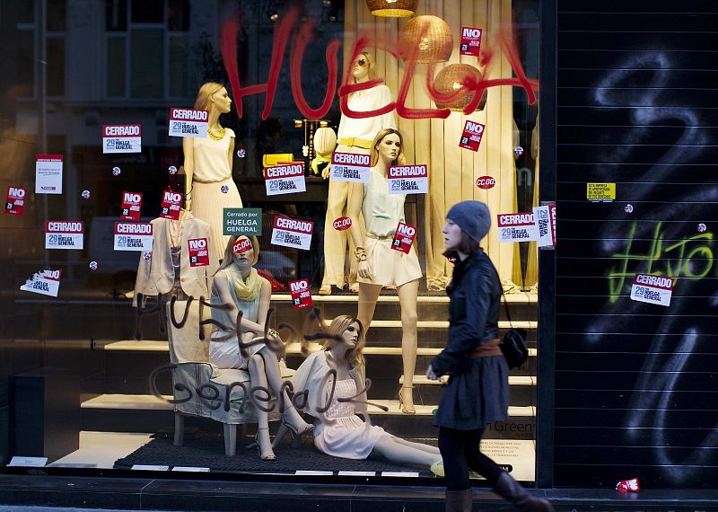 A woman walks past a store window display plastered with strike stickers and graffiti during a general strike in Madrid
