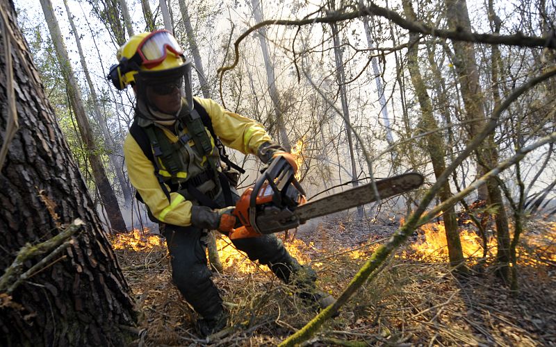 Un bombero corta ramas con una motosierra.