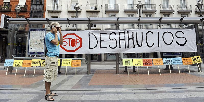 Un joven conversa por teléfono en la Plaza de Fuente Dorada de Valladolid delante de una hilera de pancartas reivindicativas del movimiento 15M.