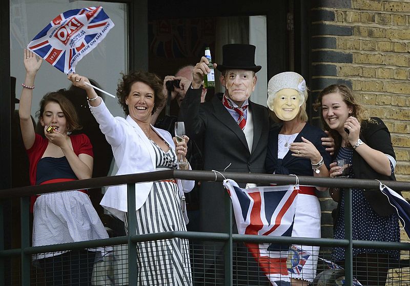 People wearing masks of Britain's Queen Elizabeth and Prince Philip wave while watching a pageant in celebration of the Queen's Diamond Jubilee in London