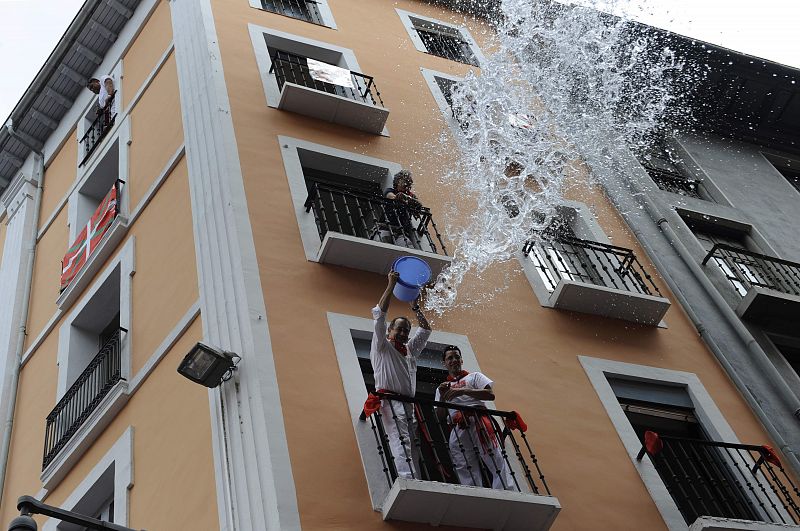 Un hombre arroja agua desde un balcón a los asistentes al Chupinazo de los Sanfermines